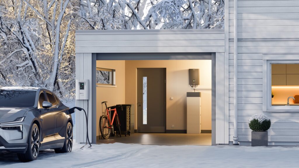 en elektrisk bil laddar med en kabel från garaget. Snölandskap och vit husfasad